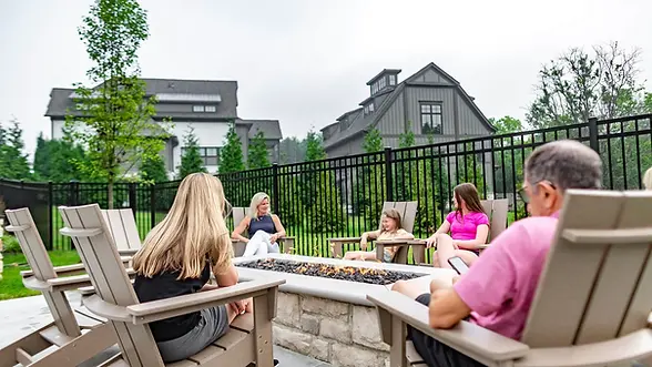 People relaxing in Adirondack chairs around a stone fire pit.