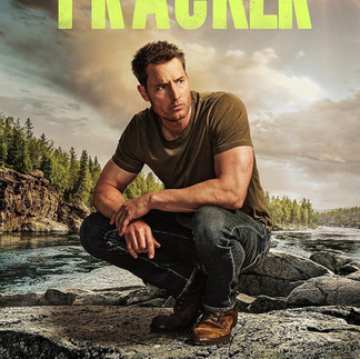 Promo shot of the main character from "Tracker" sitting outdoors in a rugged landscape, dressed in dark green casual clothes.