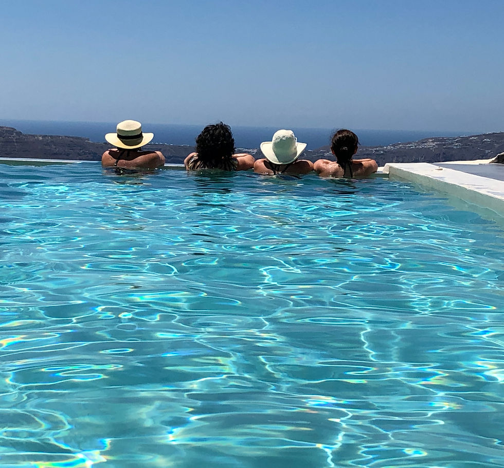 4 women looking at to the coast of Santorini in an infinity pool