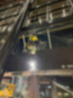 skyscraper window cleaner: Rope-access worker in yellow cleans a glass facade at night, hanging from blue ropes with a bucket; Drive arrow sign below.