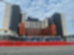 Commercial window cleaning sydney: Modern hospital campus under construction with crane, orange and gray facades, and Randwick Campus Redevelopment fencing under cloudy sky.