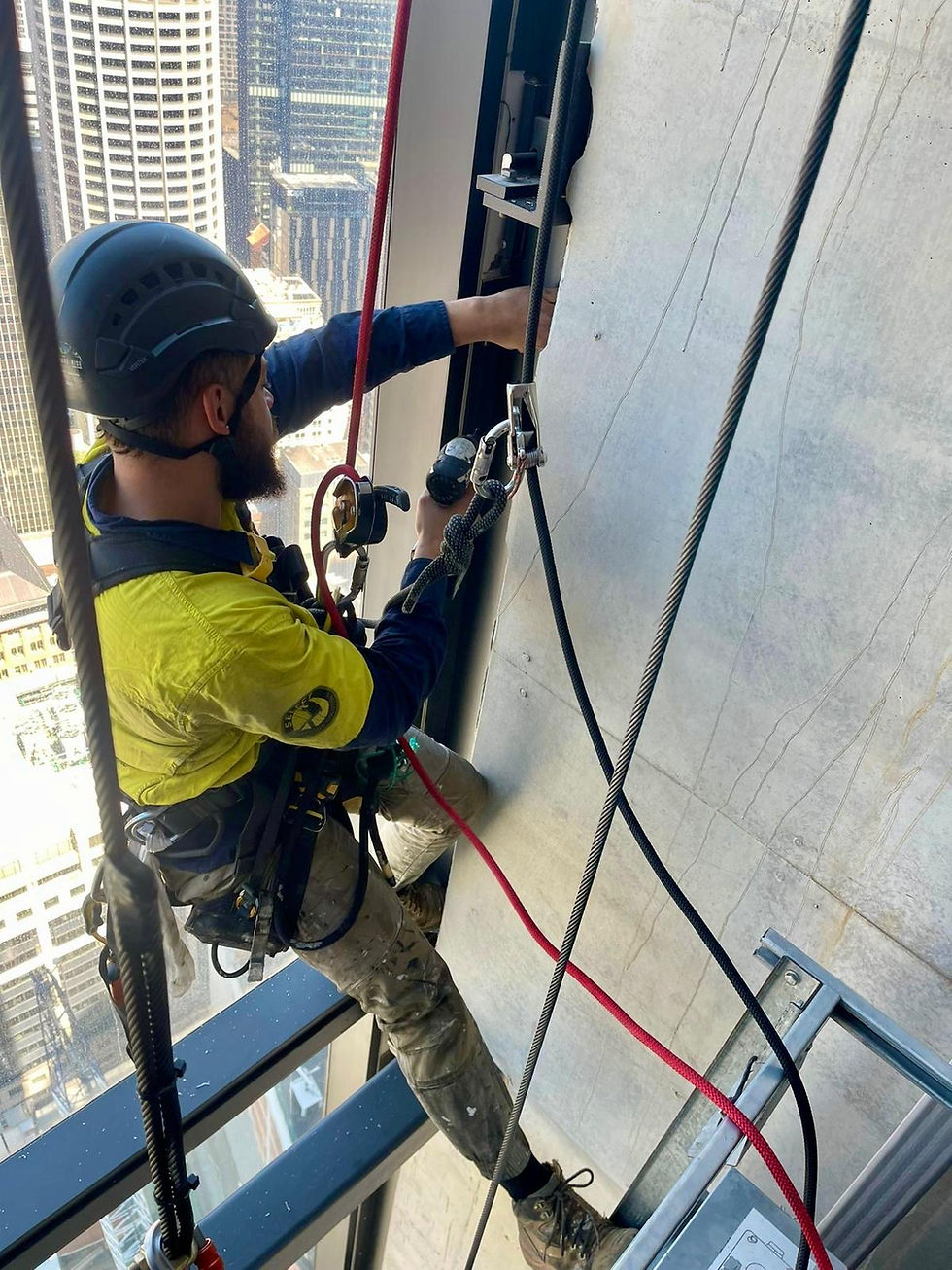 commercial window cleaning sydney: Worker in yellow and blue gear, on ropes, fixing a high-rise building exterior. Urban skyline in background. Safety harness visible.