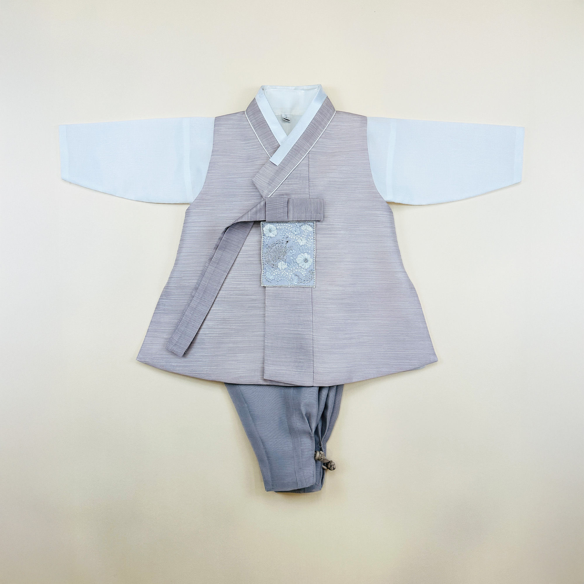 Baby boy dohl hanbok set with light mauve vest and gray pants, featuring embroidered floral pocket accent