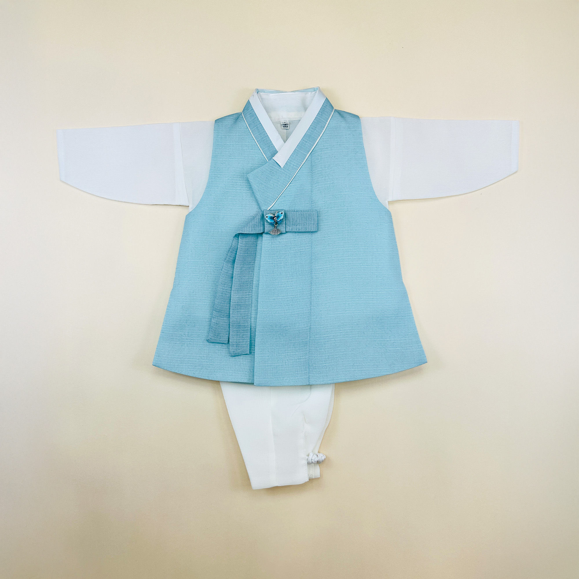 Baby boy dohl hanbok with light blue vest, white jeogori, and charcoal gray pants, accented with a decorative norigae knot
