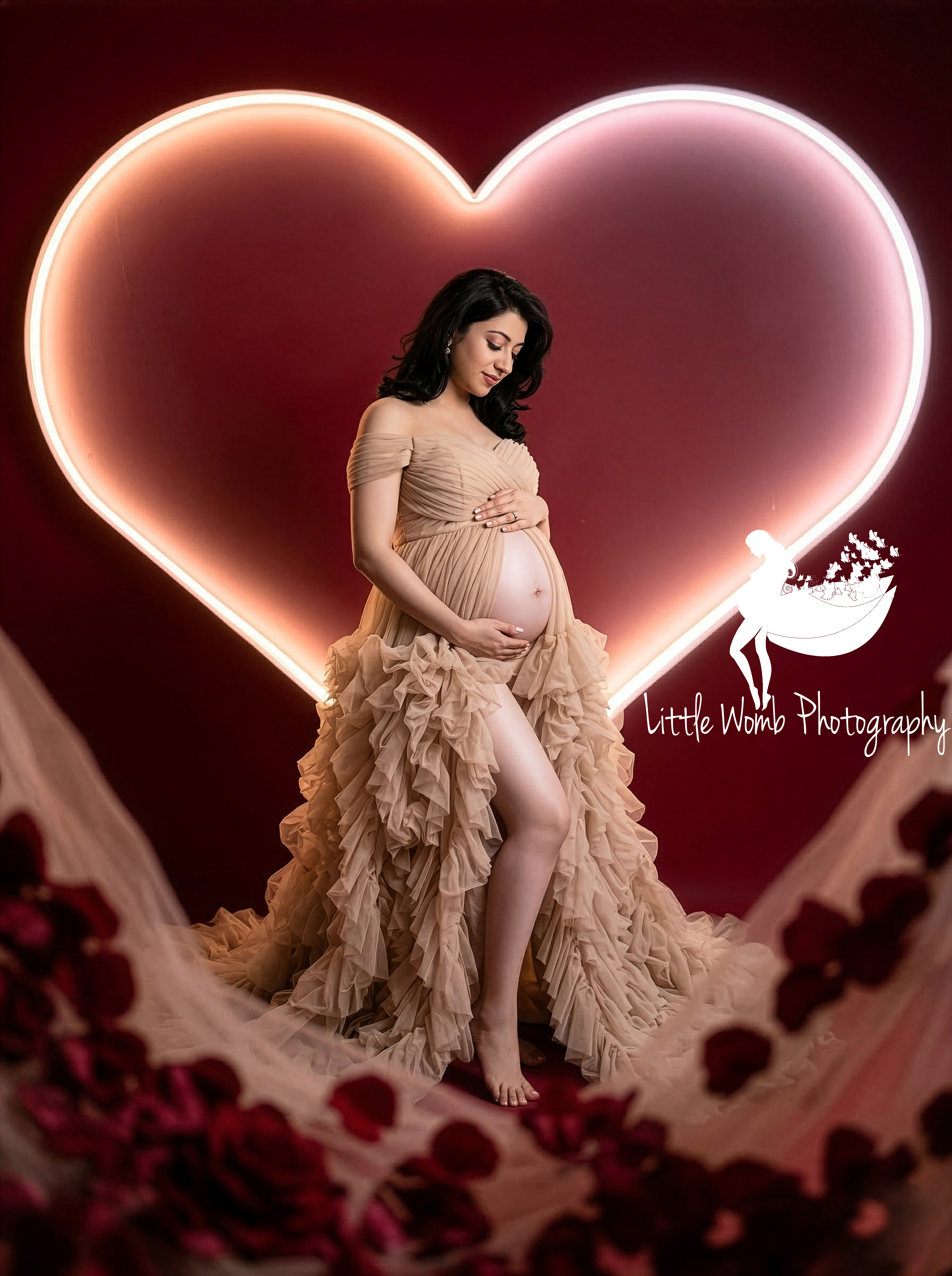 Pregnant woman in a beige tiered gown standing inside a large glowing neon heart prop for a creative maternity photoshoot in Bangalore.