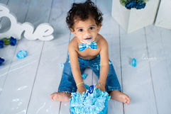 Baby boy in denim outfit smashing his first birthday cake.
