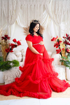 Pregnant woman in a vibrant red ruffled gown, posing with her baby bump in a studio.