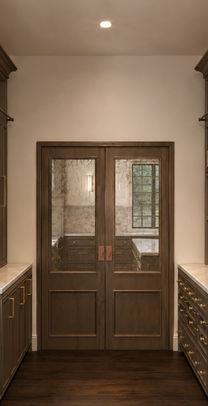 Butler’s pantry with dark custom cabinetry, brass hardware, stone countertops, open shelving, and glass-paneled wood doors.