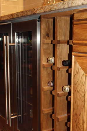 Close-up of custom vertical wine bottle storage beside a glass-front beverage refrigerator and wood cabinetry.