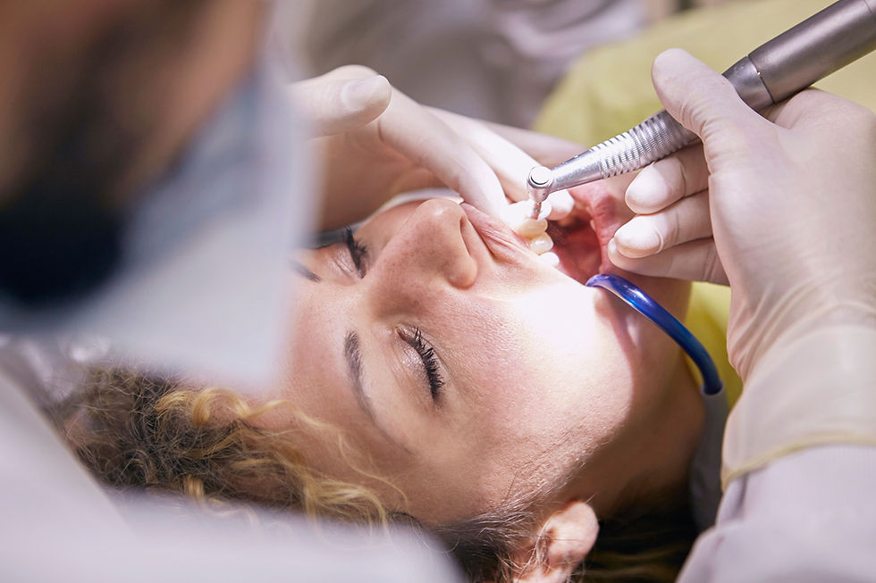 Dentistă tratează un pacient întins pe scaun, folosind freza dentară și aspiratorul, cu mănuși albe; atmosferă clinică.