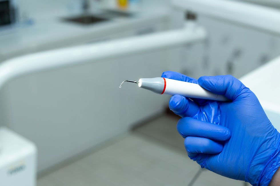 Mână cu mănușă albastră ține un instrument dentar alb într-un cabinet stomatologic, pe fundal blurat.