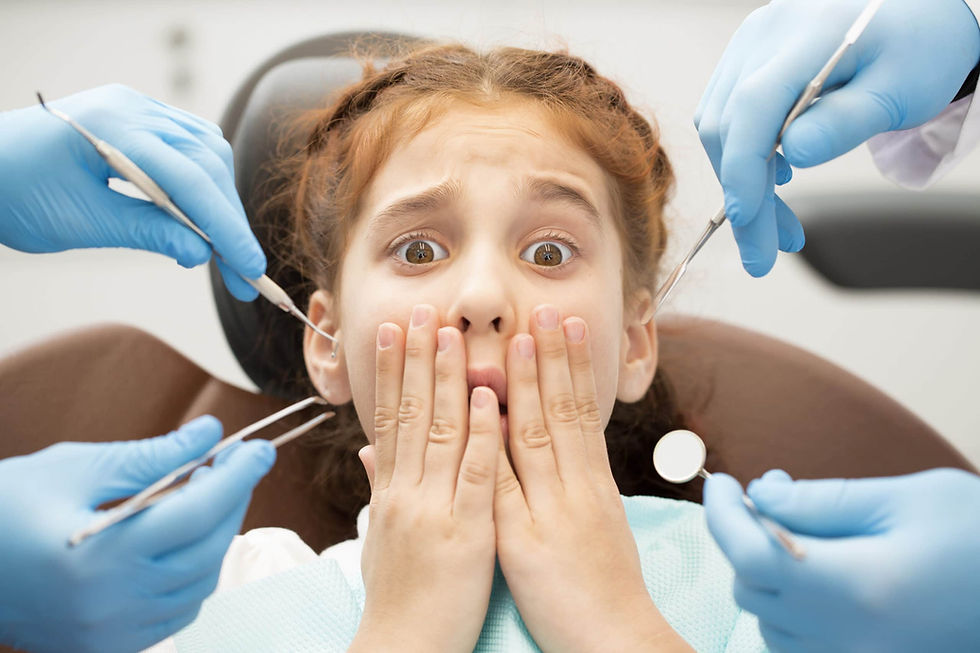Copil speriat la dentist, cu ochii mari și mâinile la gură, în timp ce instrumente albastre se apropie.
