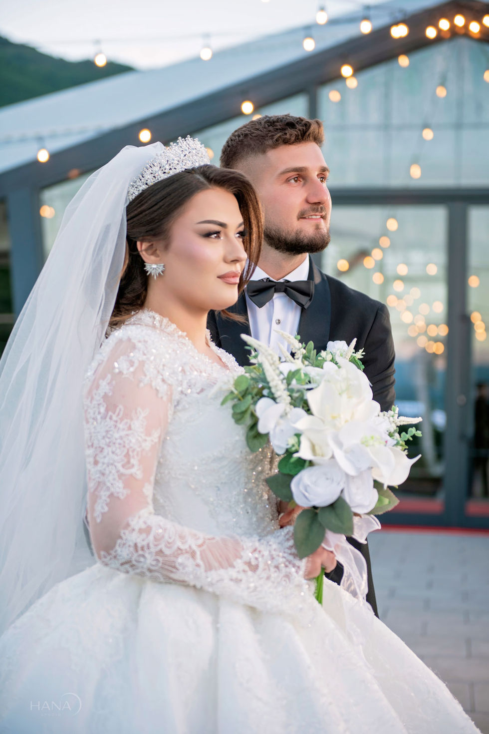 Bride and groom holding flowers, wearing formal attire.