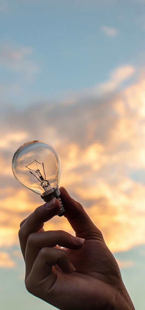 une main tient une ampoule avec en fond un ciel lumineux, symbolisant une prise de conscience