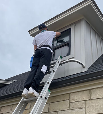 D&M Window Washing's co founder cleaning a hard to reach second story window using a squeegee and a ladder