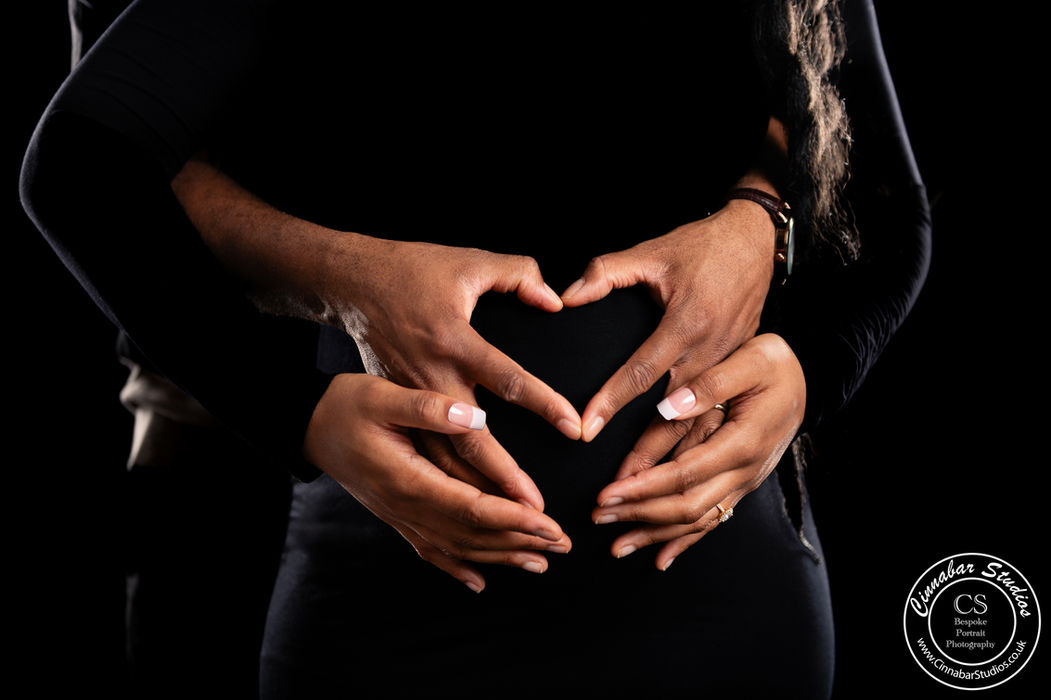 Pregnant woman and her partner make a heart over their baby during a maternity shoot
