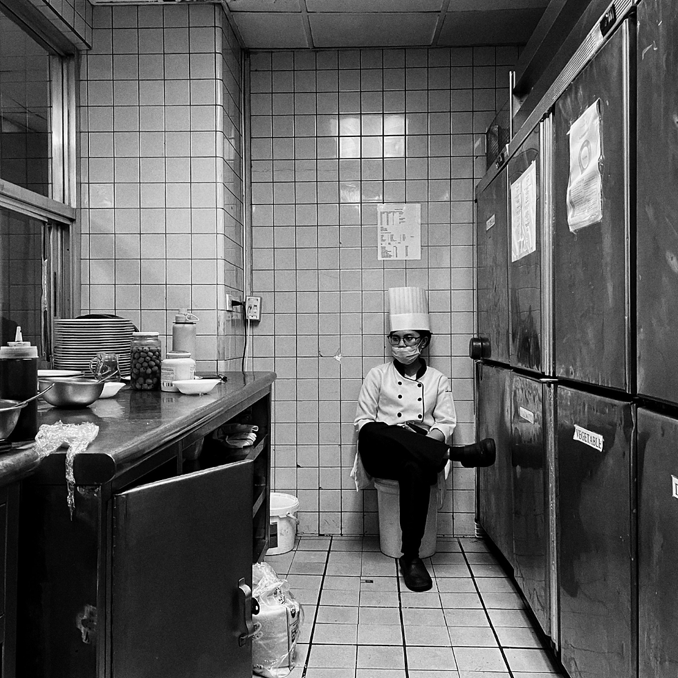 Black-and-white kitchen with a masked chef in a tall hat sitting on a bucket between counters and fridges labeled Vegetable
