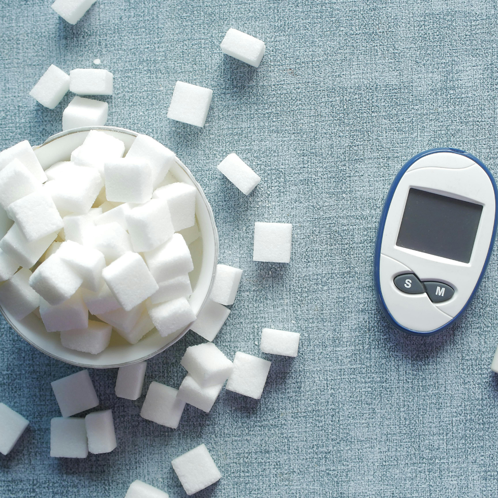 Sugar cubes spill from a bowl next to a white-blue glucose meter on a light blue fabric, symbolizing diabetes awareness.