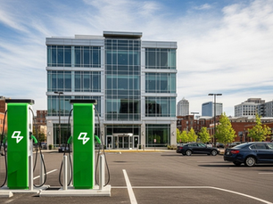 Estacionamento corporativo com duas estações de recarga para veículos elétricos em destaque, localizadas em frente a um prédio comercial de fachada envidraçada em área urbana moderna.