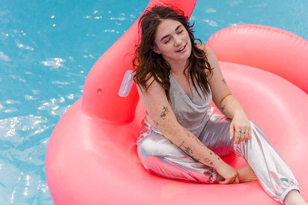 Woman in silver outfit relaxing on a pink inflatable in a pool. Sunlit, calm atmosphere, visible tattoos, no text.