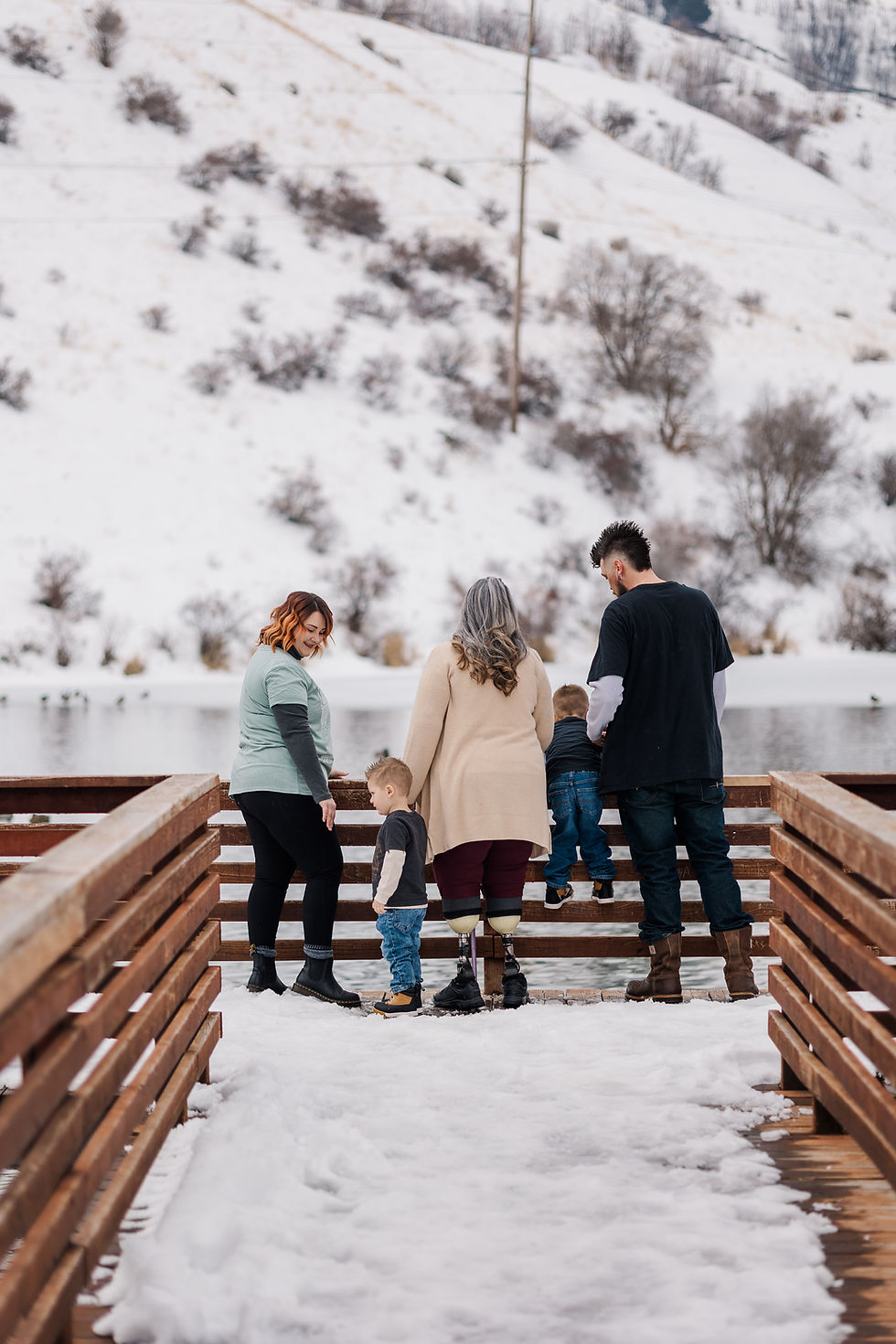 Family of five on a snowy dock by a lake, three adults, two children. Snowy hills and bare trees in the background, creating a serene scene.