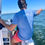 Thumbnail: Back view of man fishing on the sound in Navarre Beach wearing the NAV BCH gulf front tee in Soundside Blue color
