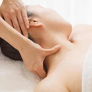 Woman laying on her back on a massage table with her head turned to the side as a massage therapist's hands can be seen massaging her neck and scalp