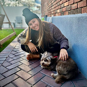 Dominika petting the family dog sitting on the ground next to her home