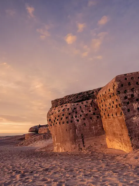 An old concrete bunker on the sand at sunset.