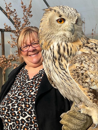 a smiling woman wearing a falconry glove while holding a western Siberian eagle owl up to the camera