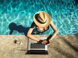 Persona revisando impuestos mientras viaja, con laptop, maleta y documentos de gastos.