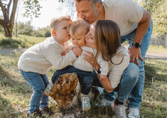 Eltern und Geschwister küssen gemeinsam ein Baby bei einem Familienshooting im Grünen