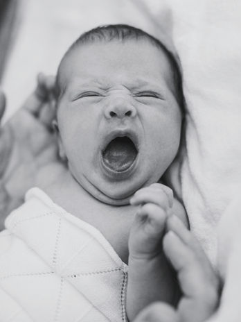 Schwarzweißes Foto eines gähnenden Neugeborenen während eines entspannten Newbornshootings.