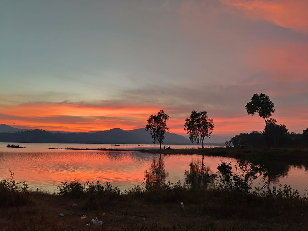 A stunning golden sunset over the Vadaj Dam reservoir in Junnar, with the Sahyadri mountain silhouettes reflecting in the water, located near Fulgulab Lawns & Homestays