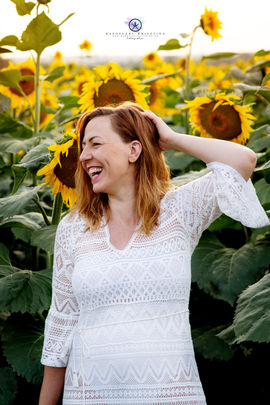 Napraforgó előtti női portré fotó miközben nevet és az egyik keze a hajába túr