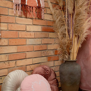 Enterőr rózsaszín és natúr színekkel, rúzsaszín és fehér díszpárnák a földön, téglafallal és egy fali képpel.