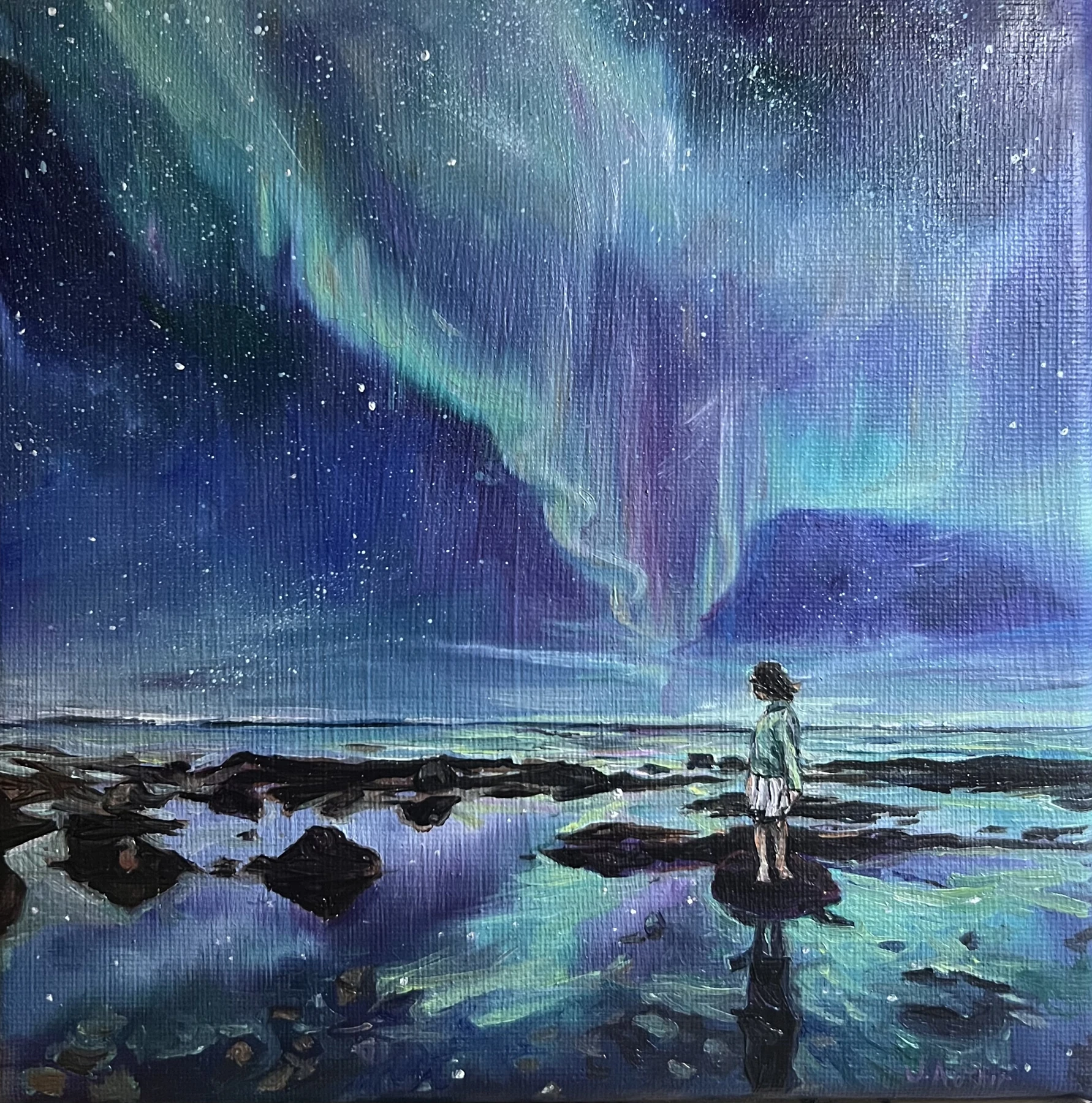 Green and violet northern lights reflected along a dark shoreline