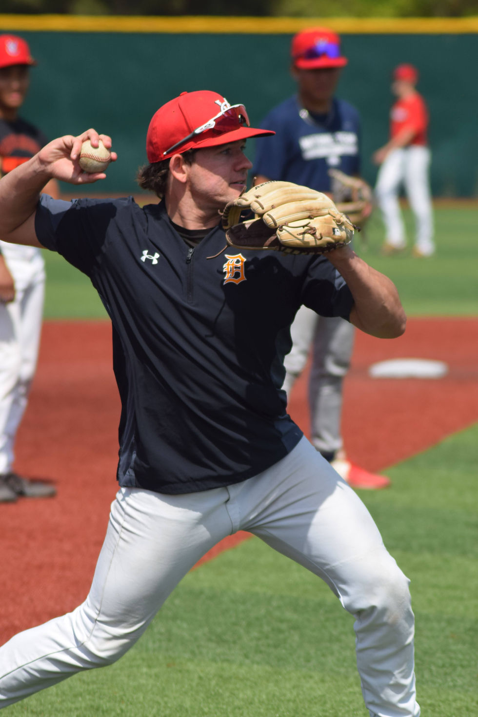 Thomas Keller, with with a slight grimace of effort under a red VC hat, levels his shoulders for balance and strides towards his target as he begins a throw from third base.