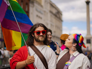 A man dressed as Jesus poses with a lady, whilst holding a pride flag.