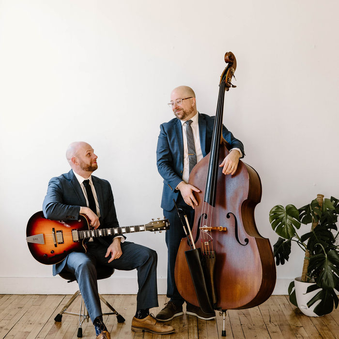 professional jazz musicians wearing matching suits and posed in front of their instruments, an upright bass and an acoustic guitar