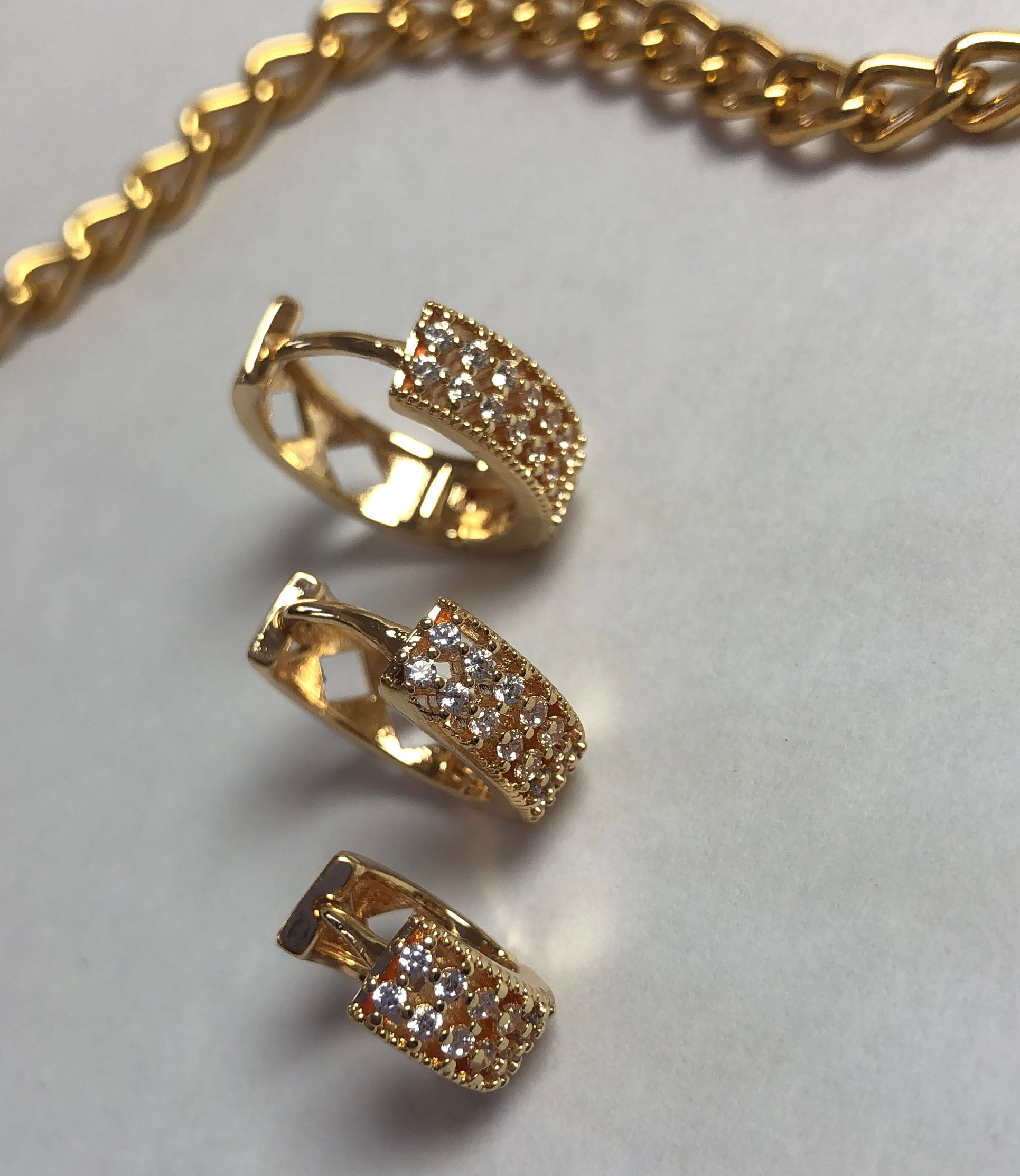 Brincos de argola dourados com pedras brancas em superfície clara.