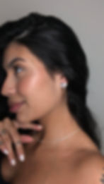 Mulher sorrindo perfil, cabelo escuro, com brincos e colar delicado.