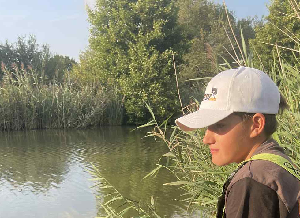 A boy fishing with a pole in the margins of a lake at Revels