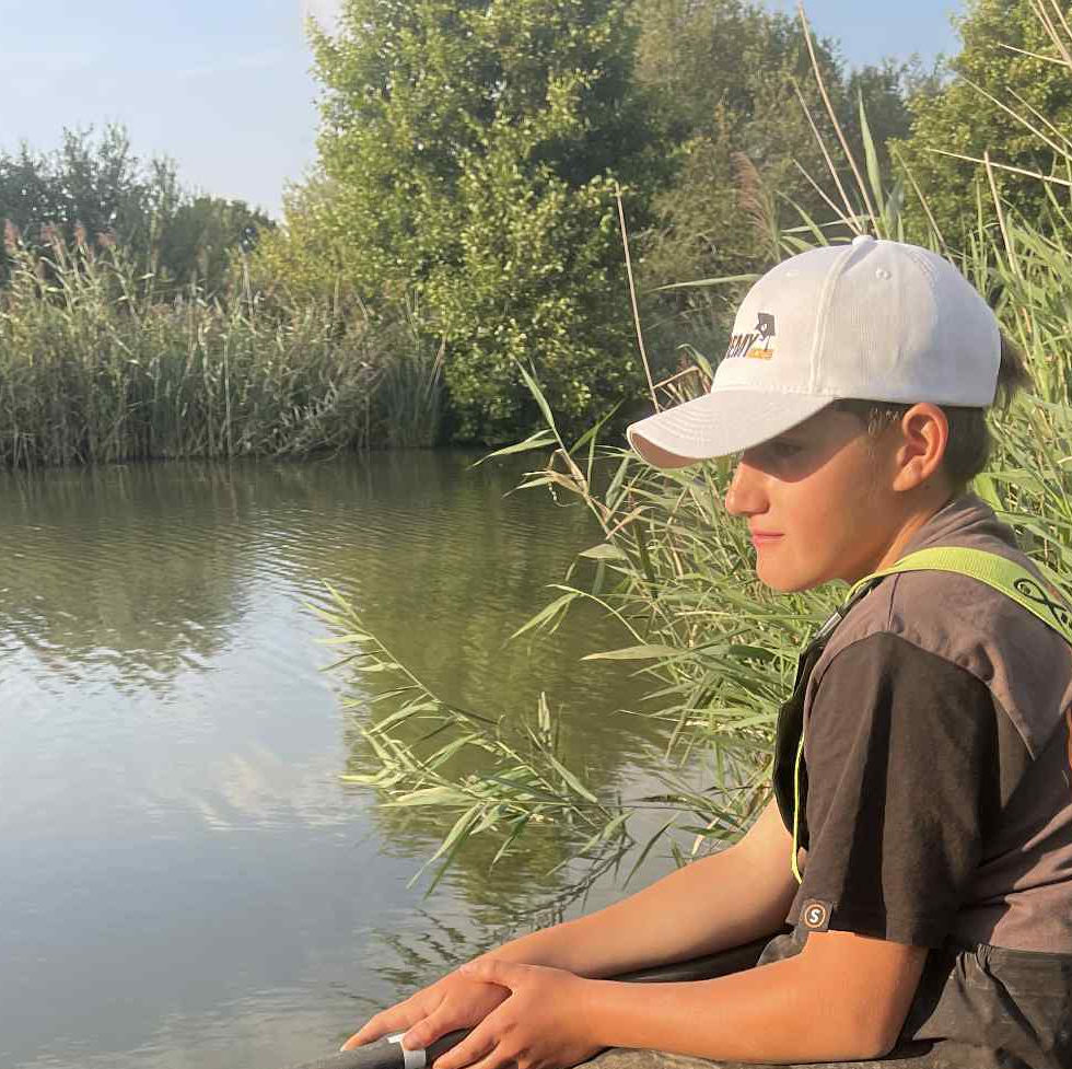 A boy fishing with a pole in the margins of a lake at Revels