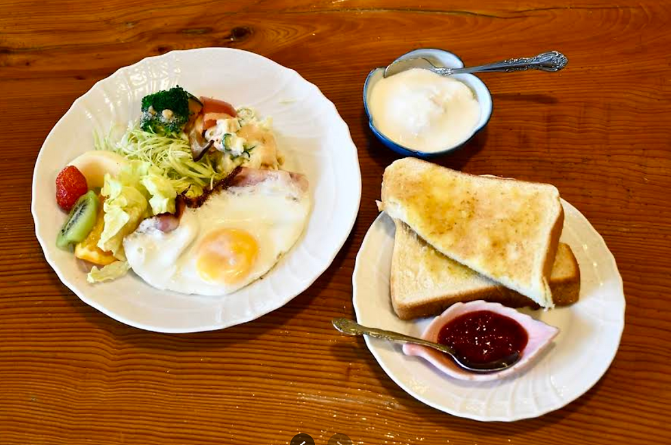 木のテーブルの上に、目玉焼きやサラダ、トースト、ヨーグルトが並んだ喫茶店のモーニングセットの写真。