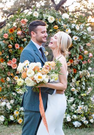Bride and groom surrounded by florals of white orange and yellow roses at their wedding at The Wayback in austin texas