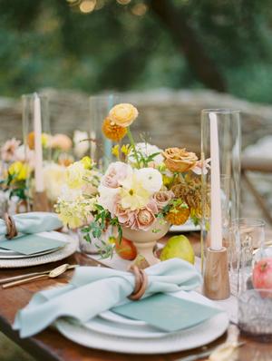 wedding reception table details of blue napkins and fall colored florals with pink taper candles