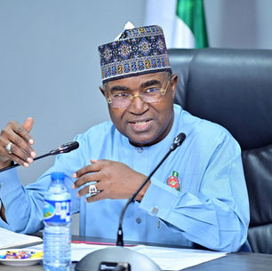 Brigadier General Mohamed Buba Marwa seated at a conference table, wearing traditional Nigerian attire and cap, speaking into a microphone during an official security meeting, with documents and a water bottle visible, reflecting senior leadership and formal engagement.