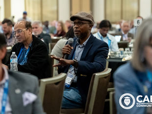Dr. Sunday Oludare Ogunlana speaks into a microphone from the audience during a session at the 2026 CAE in Cybersecurity Community Symposium.