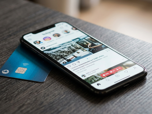 A smartphone showing a social media app beside a bank card, illustrating the merger of social identity and digital payments.